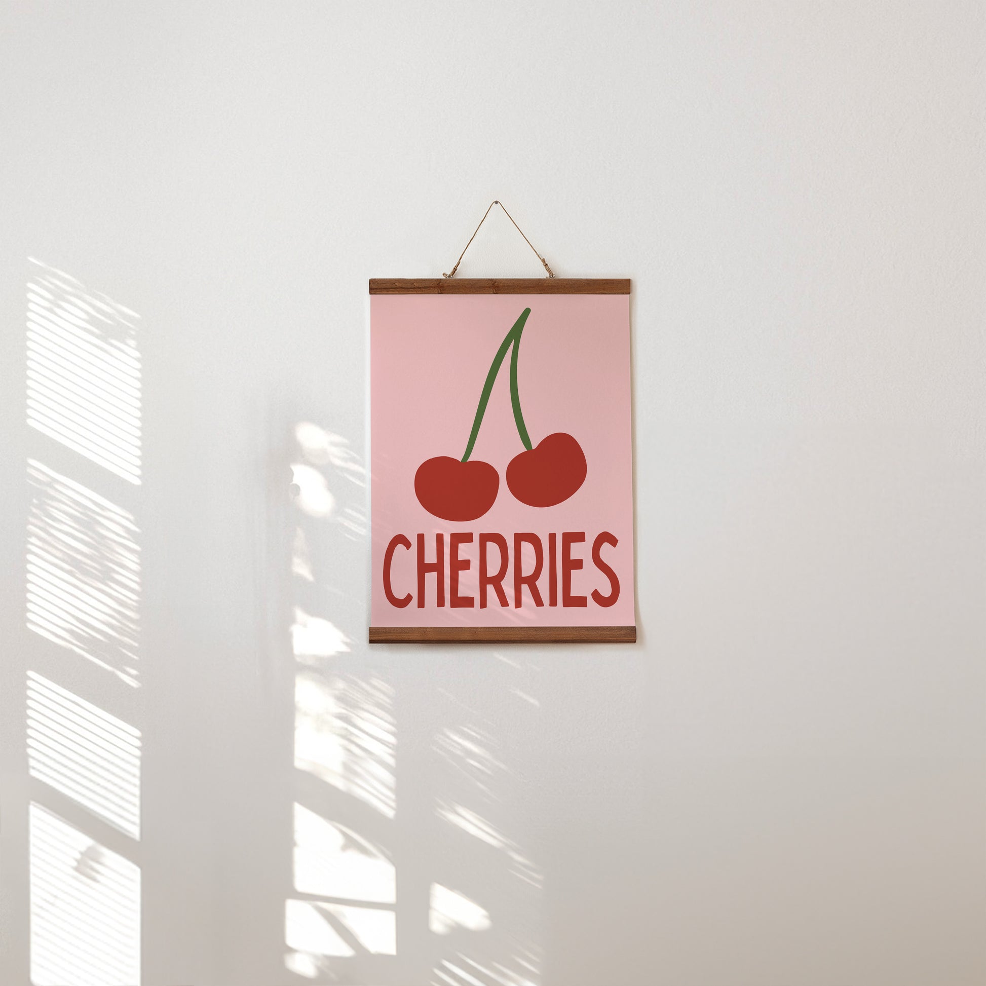Poster with 'CHERRIES' text and cherry illustration on a pink background, hanging on a white wall.