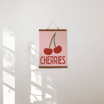 Poster with 'CHERRIES' text and cherry illustration on a pink background, hanging on a white wall.
