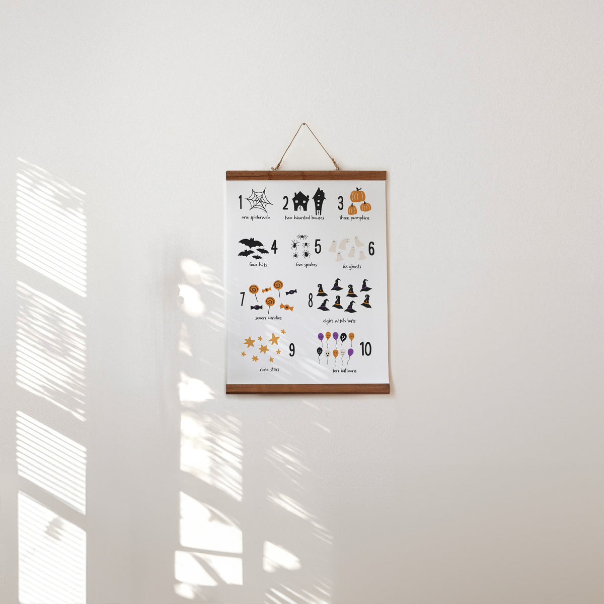 Halloween educational hanging poster with numbers and cute spooky illustrations hanging on a white wall.