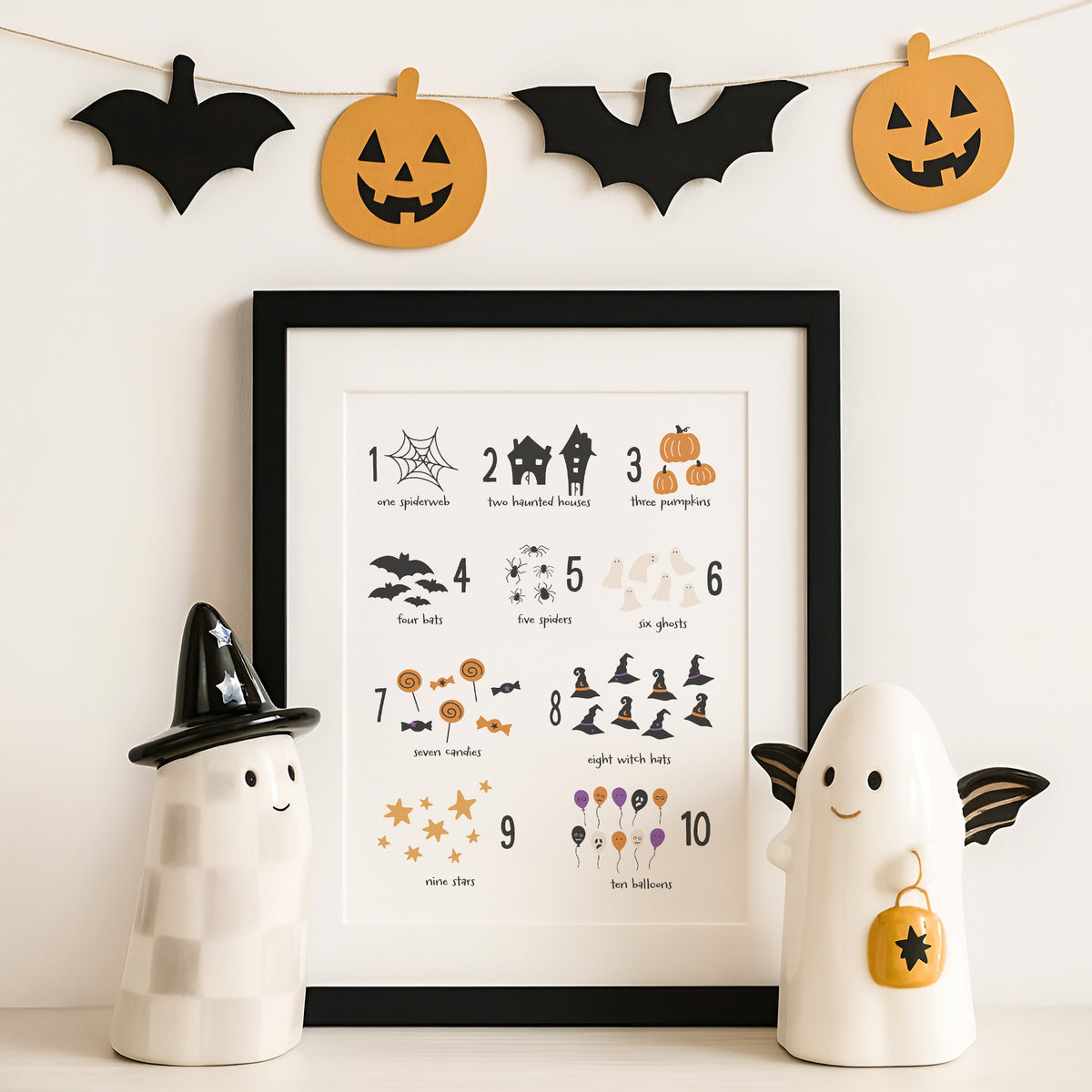 Halloween-themed decorations including a framed print, ghost and witch hats, and pumpkins on a white wall.